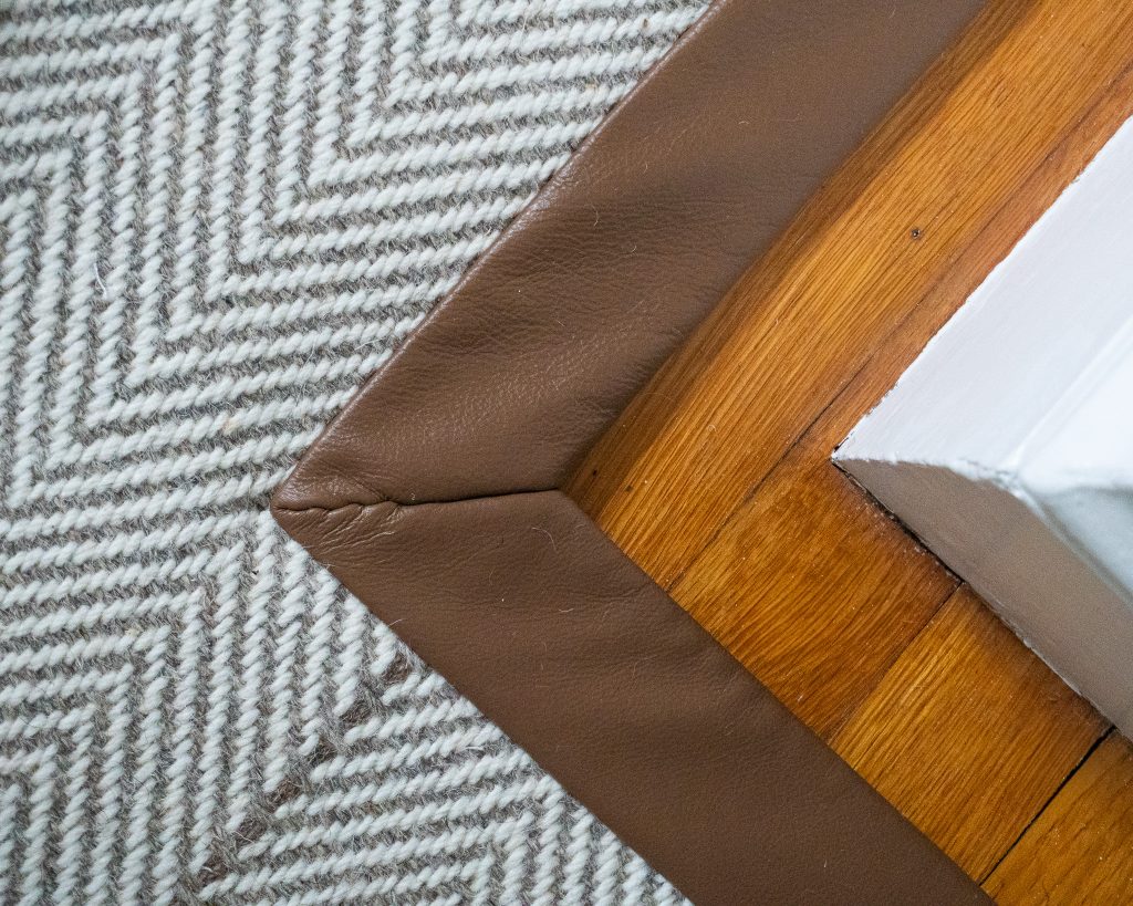 Cus0tom wool rugs can be personalized with an edge finish, like this one that has aa herringbone rug, made with wool, and finished with a leather wide binding.