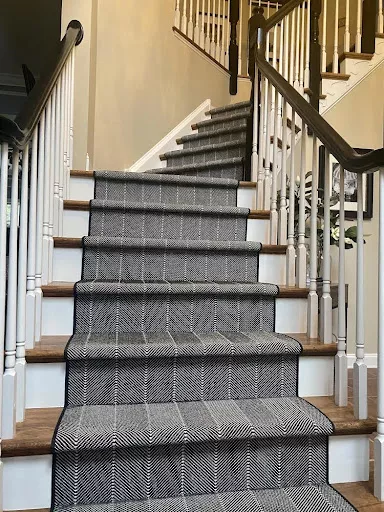 Dark colors on a carpet with a herringbone style and a narrow black binding fabricated and installed as a stair runner.