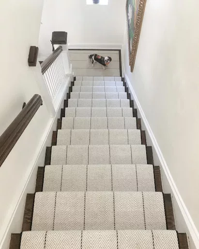 White carpet with a cheveron style and a narrow black binding fabricated with no-toxic elements and installed as a stair runner.