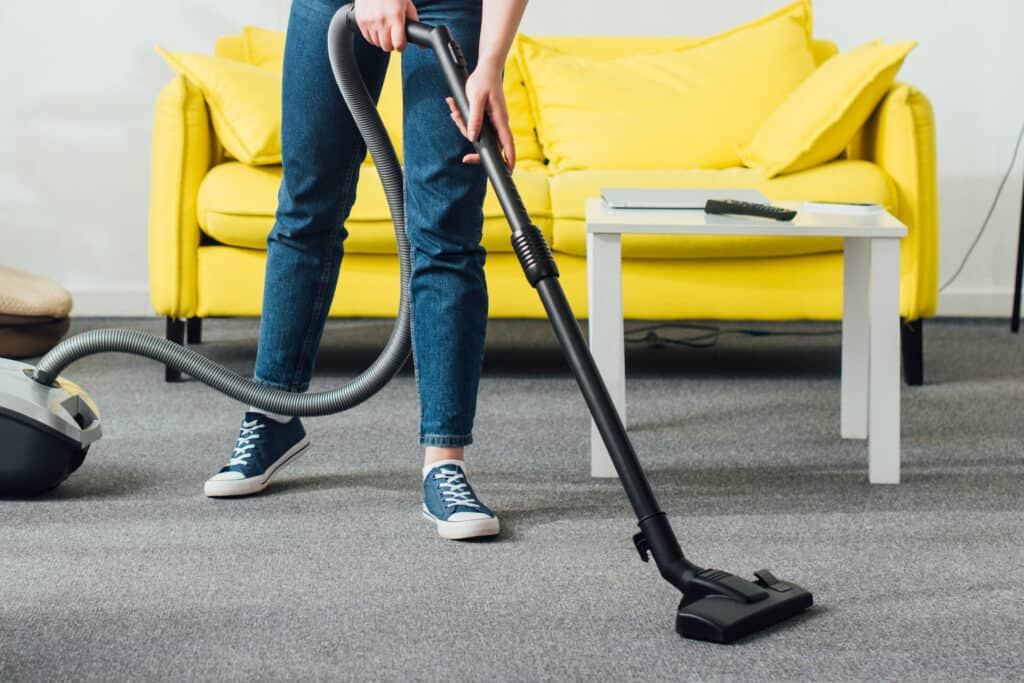 Smiling woman cleaning carpet with vacuum cleaner in living room