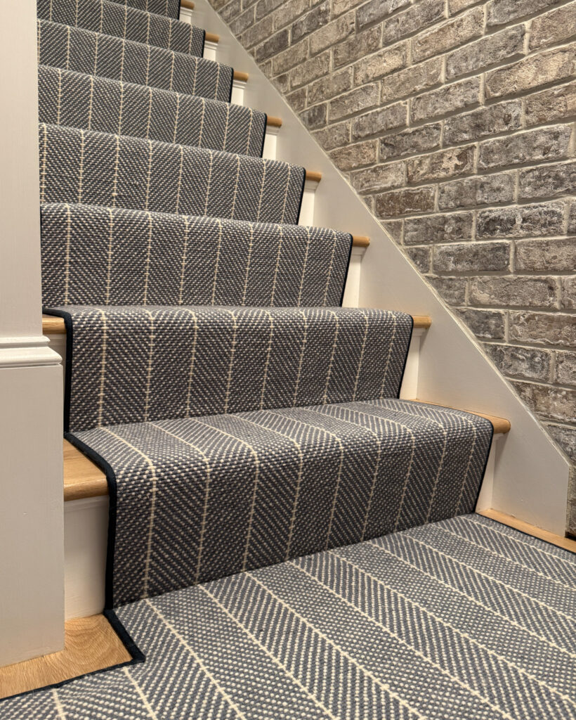 Dark blue stair runner in basement space with brick walls. Installed using waterfall style.